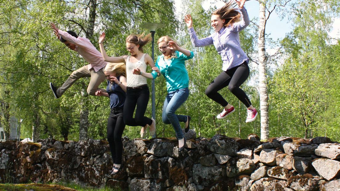 Viisi nuorta hyppää ilmaan kivimuurilta.