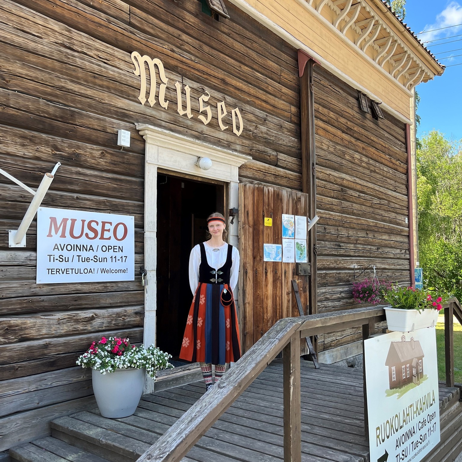 nuori tyttö seisoo vanhan puisen museon oven edessä kansallishameessa 